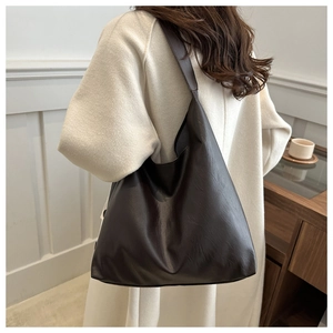Detail of dark brown leather tote bag with wide shoulder strap worn by a model