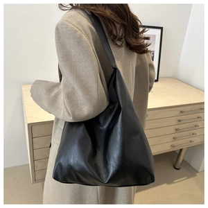 Large black leather tote bag worn by model in beige coat, minimalist retro shoulder bag style