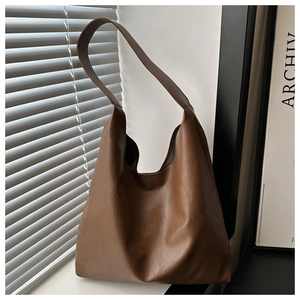 Detail of soft brown leather tote bag with wide strap by a sunlit shutter window