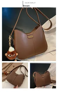Detailed close-up of brown PU leather crossbody bag with logo and monster plush charm