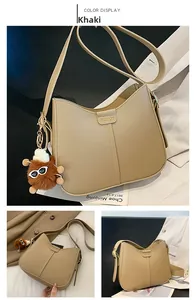 Detail of khaki crescent leather shoulder bag with fashion logo and brown plush charm