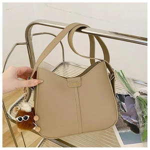 Detail view of khaki leather bag with FASHION buckle and plush charm on a rack