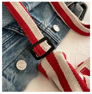 Detail of blue denim fabric with red-white striped strap and silver JEANS metal button