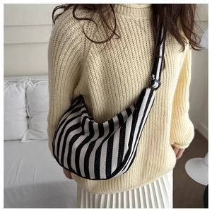 Close-up of a striped half-moon canvas shoulder bag with adjustable strap on a model