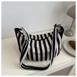 Detail of black and white striped canvas crossbody dumpling bag on a minimalist white desk