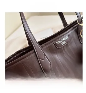 Detail of dark brown tote bag featuring wavy embossed texture and golden metal hardware