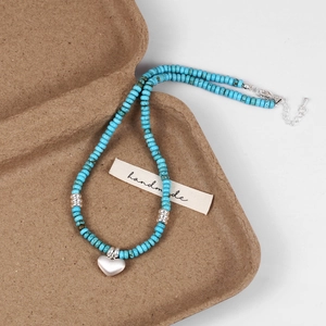 Detail of handmade turquoise beaded necklace with heart pendant on paper gift box
