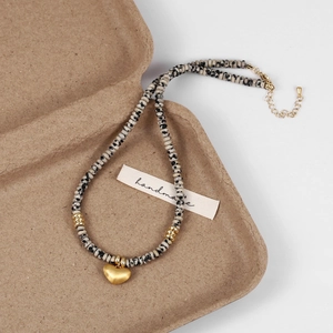 Macro view of spotted natural stone beads and gold heart pendant on handmade necklace