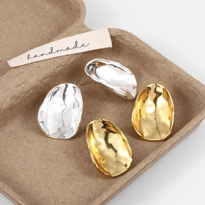 Macro shot of irregular wavy oval stud earrings in polished gold and silver metal