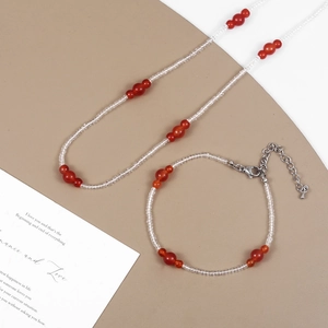 Detail view of a red agate and white beaded necklace and bracelet set on a beige background