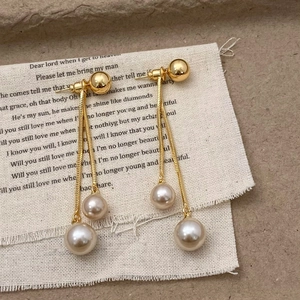 Detail shot of champagne pearl tassel earrings on a textured stone and fabric background