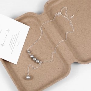 Detail of adjustable Y-shaped silver necklace with five grey pearls on a paper tray