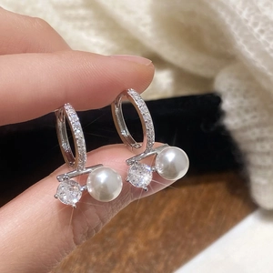 Macro shot of silver pearl hoop earrings with zircon pavé detail held by hand