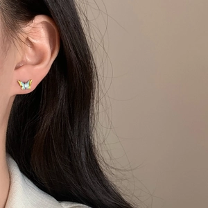 Gros plan détaillé d'une boucle d'oreille papillon bleue dorée avec zircon sur l'oreille