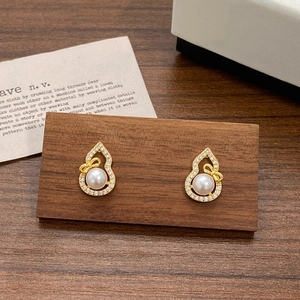 Elegant gold hulu earrings with pearls and bow details on wooden display stand
