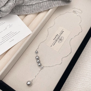 Elegant silver tassel sweater necklace with five grey pearls on a beige textured background