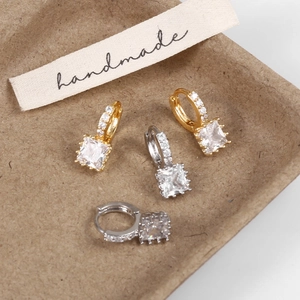 Close-up of gold and silver square zircon hoop earrings on a handmade fabric label