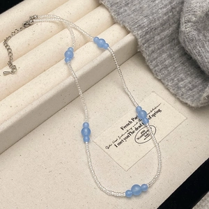 Beaded necklace with light blue stone charms and transparent beads on a neutral display