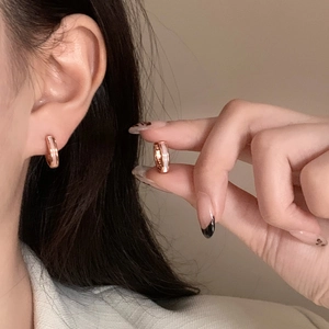 Détail de créoles en or rose avec nacre blanche montrées sur l'oreille et la main