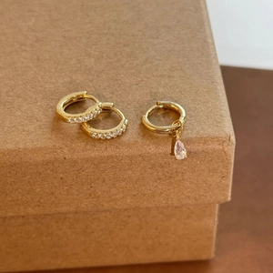 Close-up of gold asymmetrical hoop earrings with micro-pave crystals and teardrop pendant