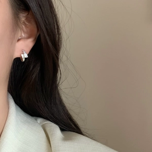 Close-up of geometric silver earrings with pavé crystals worn on a model's ear