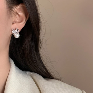 Close-up of bow knot pearl earrings with sparkling zircons on a model's ear