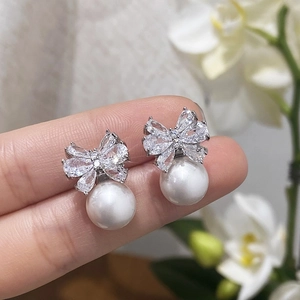 Bowknot pearl earrings with sparkling zircons and silver finish held by hand