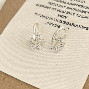 Close-up of silver flower earrings with micro-set zircons on white texture card
