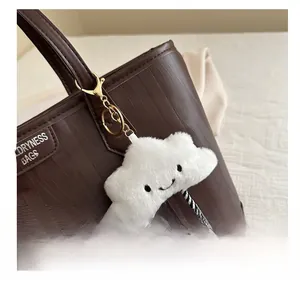 Detail of a white fluffy cloud charm with smiling face hanging on a brown leather tote bag
