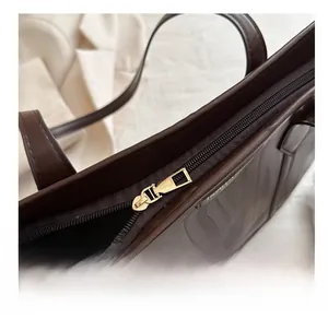 Detail showing smooth gold metal zipper and premium brown leather texture on the tote bag