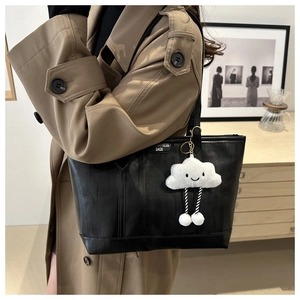 Detail of black leather tote bag with white cloud charm on a model in trench coat