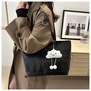 Detail of black striped tote bag with plush cloud charm worn by a model in a trench coat