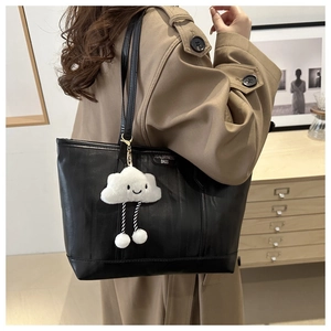 Detail of black tote bag with textured finish and cute white cloud plush pendant