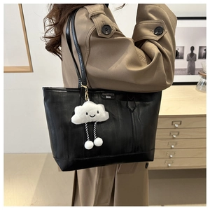 Detail of black leather tote bag with white plush charm and slim shoulder straps