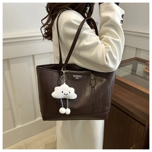Detail of deep brown tote bag with leather texture and cute cloud charm on white coat
