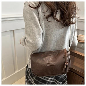 Detail of a dark brown crossbody bag featuring a textured finish and fashion leather tag