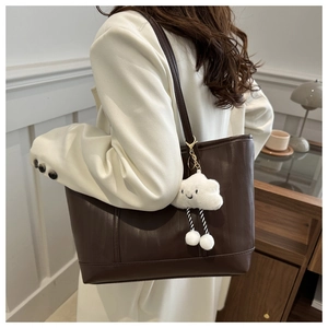 Detail of dark brown leather tote bag with embossed texture and white cloud plush charm