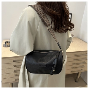 Detail of black Boston bag with bohemian wide strap and fringe on a model background