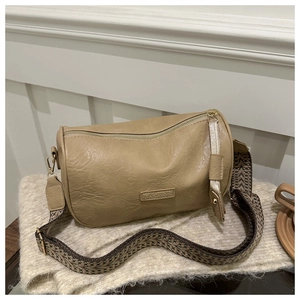 Detail of khaki cylinder bag with fashion label and wide geometric woven shoulder strap
