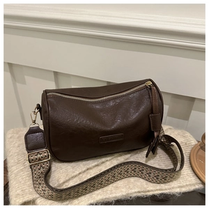 Detail of dark brown cylinder crossbody bag with wide ethnic weave strap on soft fabric