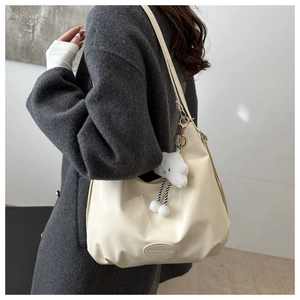 Detail view of cream white leather tote bag featuring fashion tag and cloud plush charm