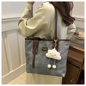 Detail of grey denim tote bag with leather straps and a white cloud plush charm
