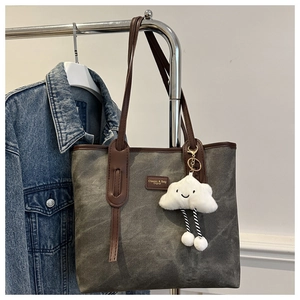 Detail view of large grey canvas tote bag with brown leather trim and plush cloud charm