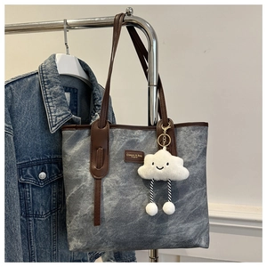 Detail of grey canvas tote with brown leather straps and cloud plush charm detail