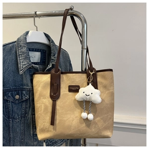 Detail of beige canvas tote bag with brown leather straps and plush cloud charm