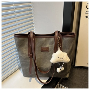 Close-up of olive canvas tote bag with brown leather handles and plush cloud charm