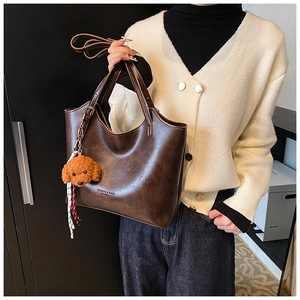Brown vintage faux leather tote bag detail with plush dog charm and shoulder strap