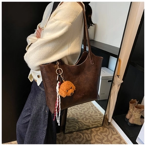 Detail of dark brown leather tote bag featuring a cute poodle plush charm and braided cord