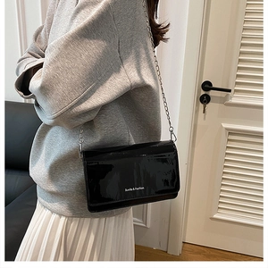 Close-up of black patent leather crossbody bag with silver chain and white logo text