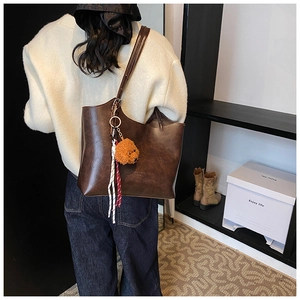Detail of dark brown leather tote bag featuring fashion embossing and a bear charm